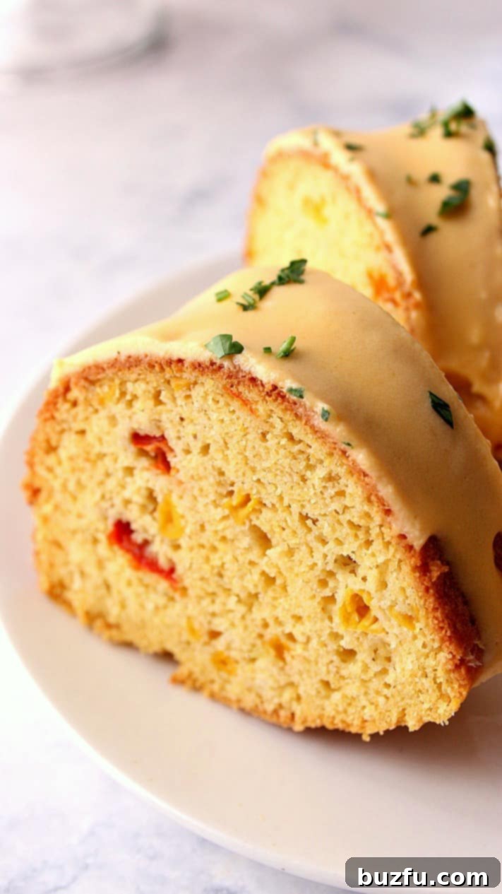 Close-up shot of a single slice of cornbread bundt cake on a white plate, showcasing its fluffy texture and golden crust, with a hint of cheese sauce.