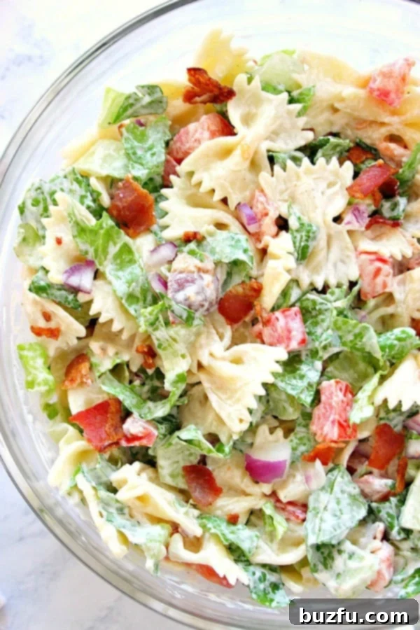 BLT Pasta Salad in large glass bowl, featuring crispy bacon, vibrant lettuce, and chopped tomatoes mixed with bow tie pasta and a creamy dressing.