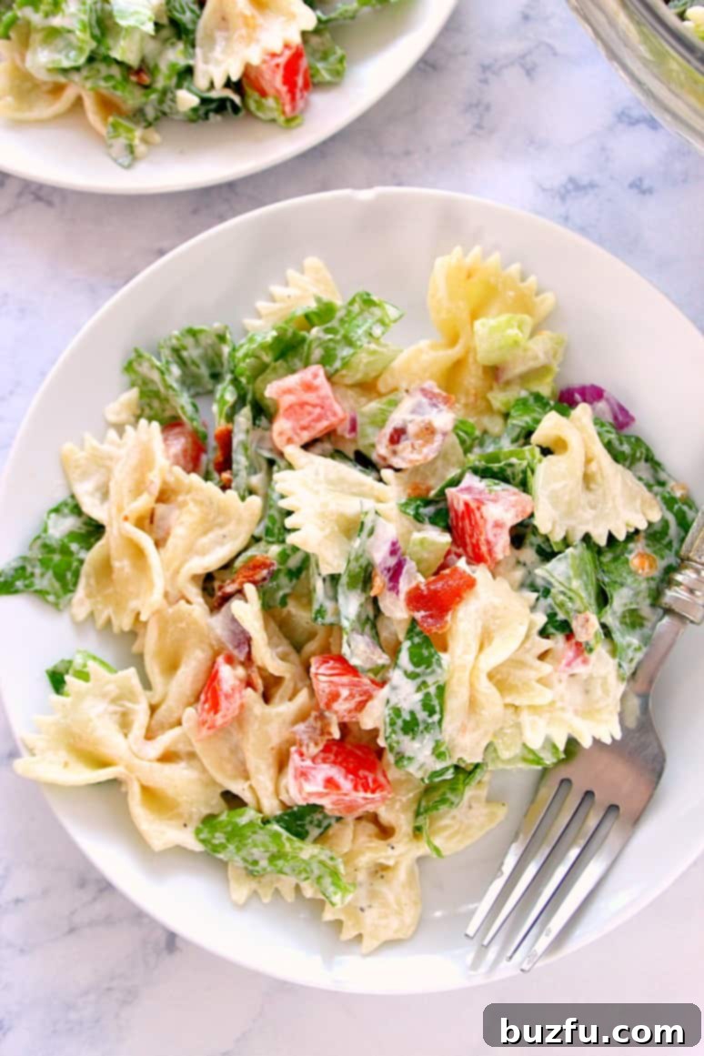Overhead shot of BLT pasta salad on white plate, with fork on side, highlighting the vibrant colors and creamy texture.