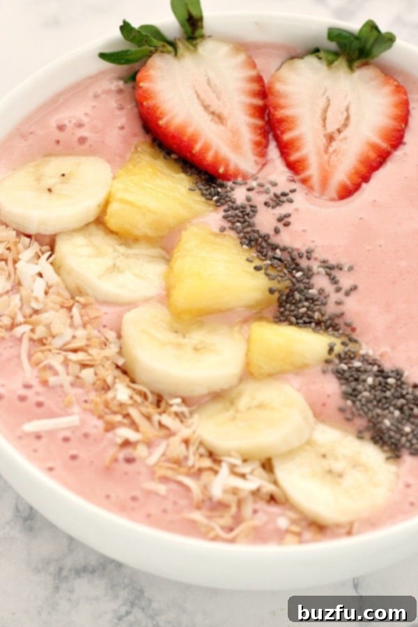 Close-up of a strawberry pineapple smoothie bowl adorned with a variety of colorful toppings, including fresh fruit, nuts, and seeds.