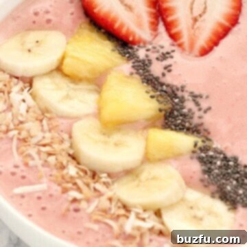 Strawberry smoothie in a bowl with pineapple and banana slices on top.