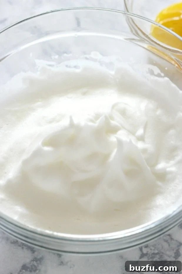 How to make low-carb keto cloud bread with high protein. An overhead shot showing perfectly whipped, glossy egg whites in a clear glass bowl, ready for the next step.