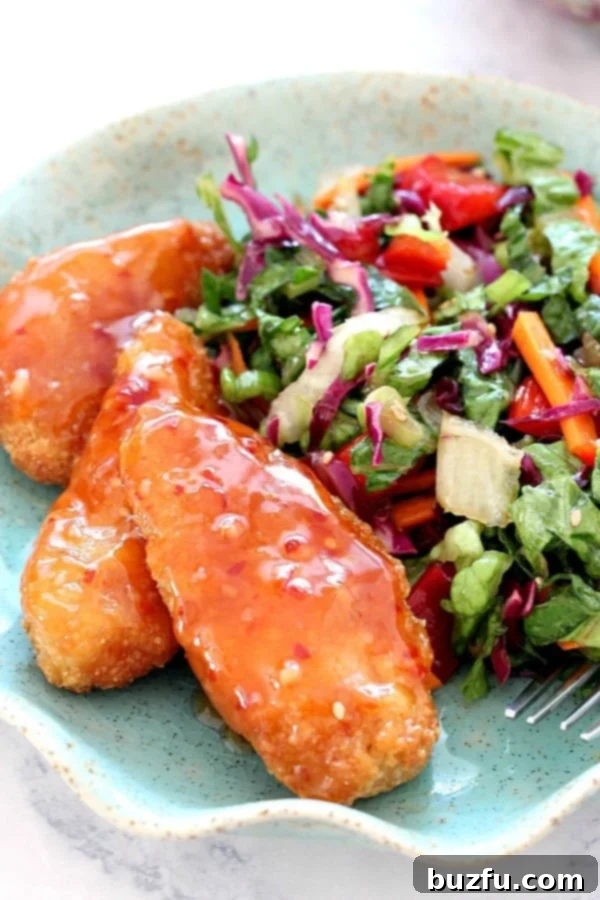 Asian Chopped Salad with Garlic Sesame Vinaigrette Recipe served with Sweet Chili Pollock Tenders - quick and easy weeknight dinner idea with a ton of flavor! A vibrant Asian Chopped Salad on a white plate, showcasing the colorful mix of lettuce, cabbage, carrots, bell pepper, and green onions, lightly dressed with a garlic sesame vinaigrette.