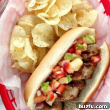 A close-up of a grilled chicken sausage in a bun, generously topped with fresh pineapple salsa and garnished with herbs.