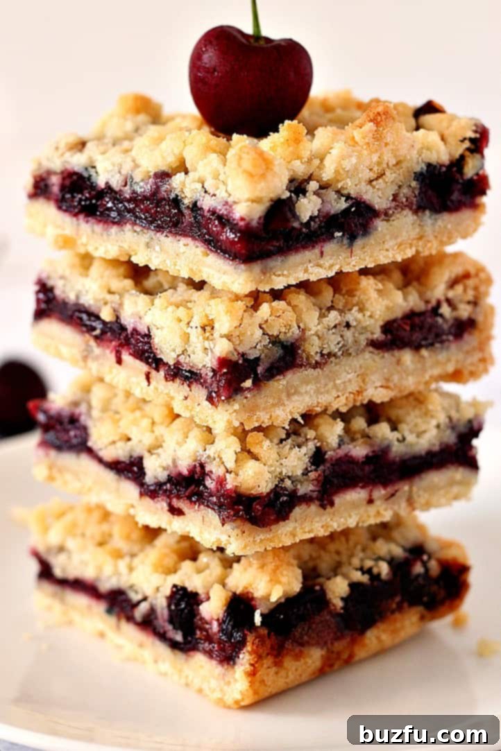 Cherry Pie Crumb Bars stacked with a fresh cherry, on a white plate, showcasing the buttery crumb topping and juicy cherry filling.