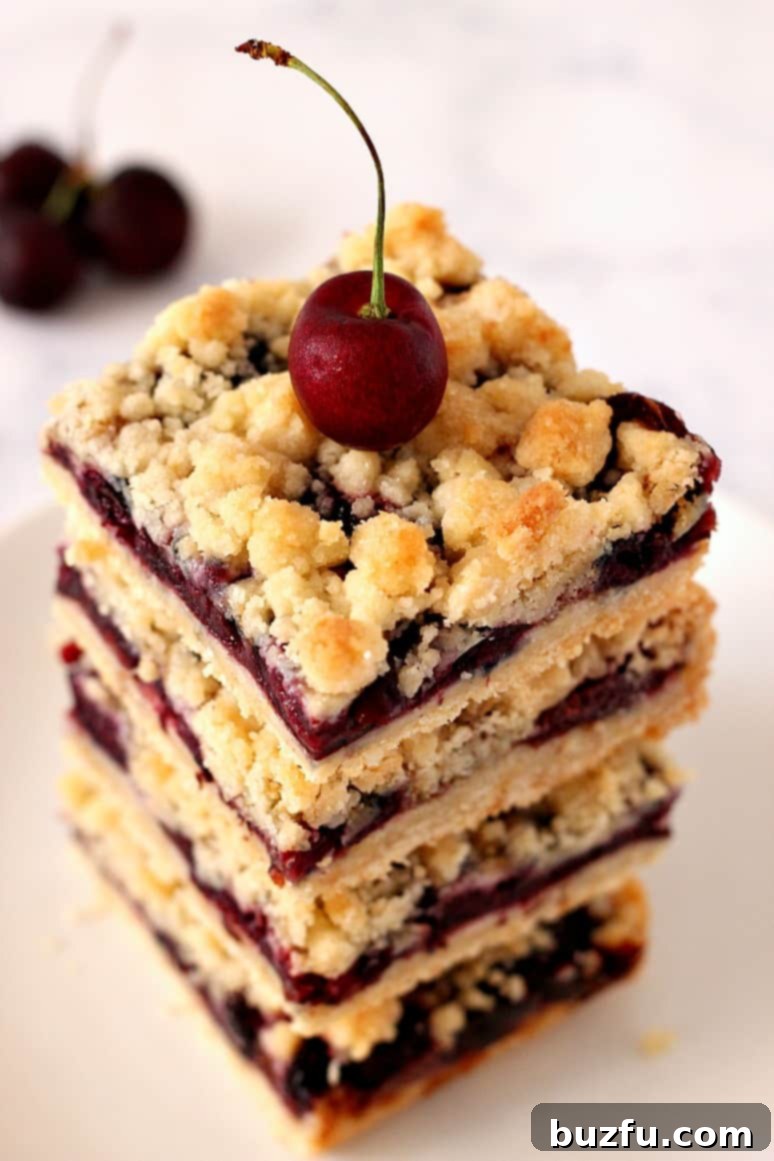 Close up of cherry crumb bars stacked with a fresh cherry on top, highlighting the crumbly texture and juicy filling.