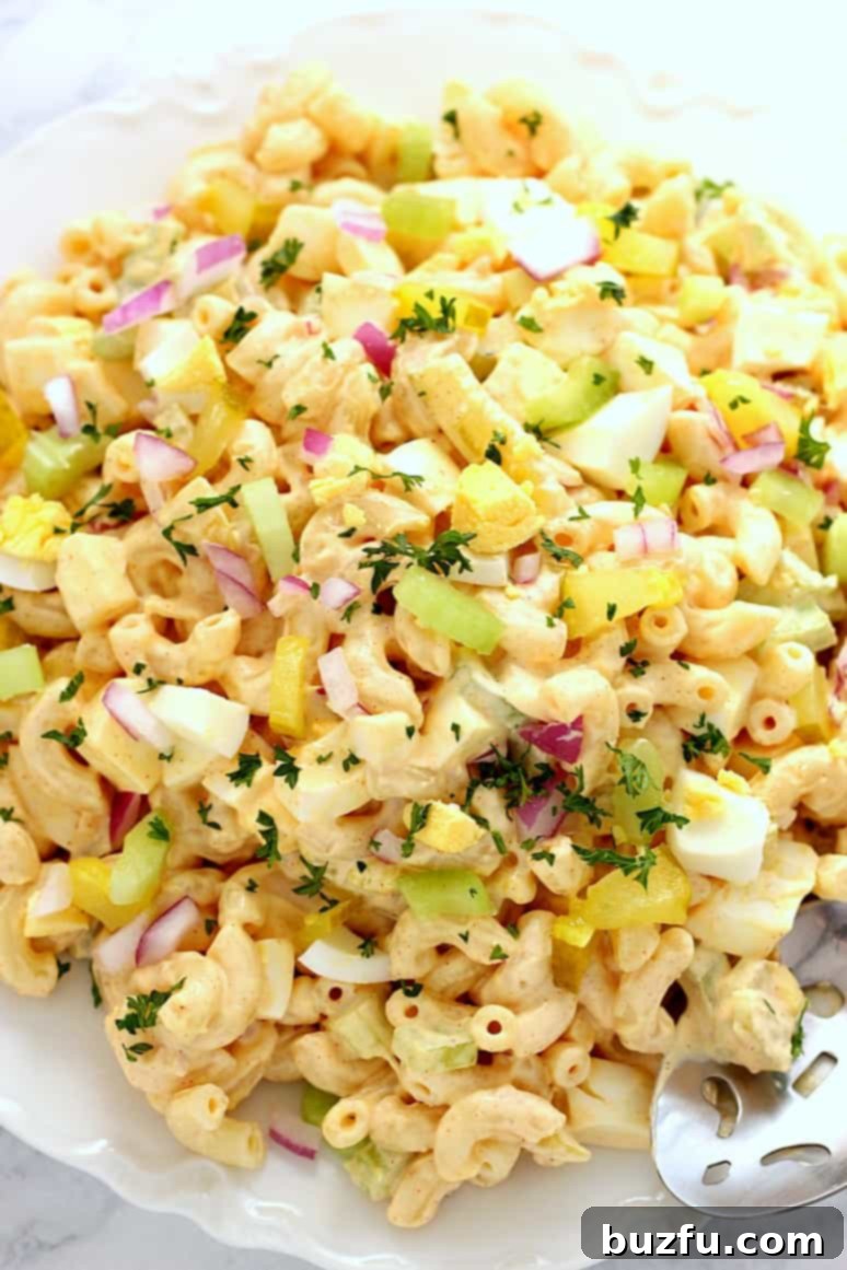 Deviled Egg Macaroni Salad Recipe - creamy pasta salad with macaroni, eggs, celery, pickles, red onion and delicious mustard paprika dressing! Close up view on a serving bowl.