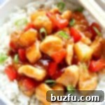 Sweet and Sour Chicken with rice in a white bowl, garnished with green onions.