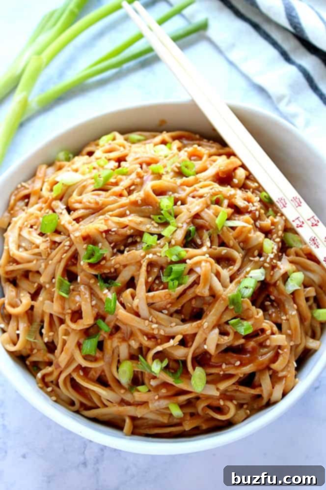 Noodles with peanut sauce and green onions in a white bowl with chopsticks, ready to eat.