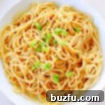 Sesame noodles in a white bowl, garnished with sesame seeds and green onions.