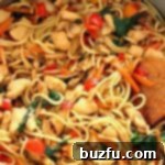 Chicken, vegetables, and lo mein noodles being stir-fried in a skillet.