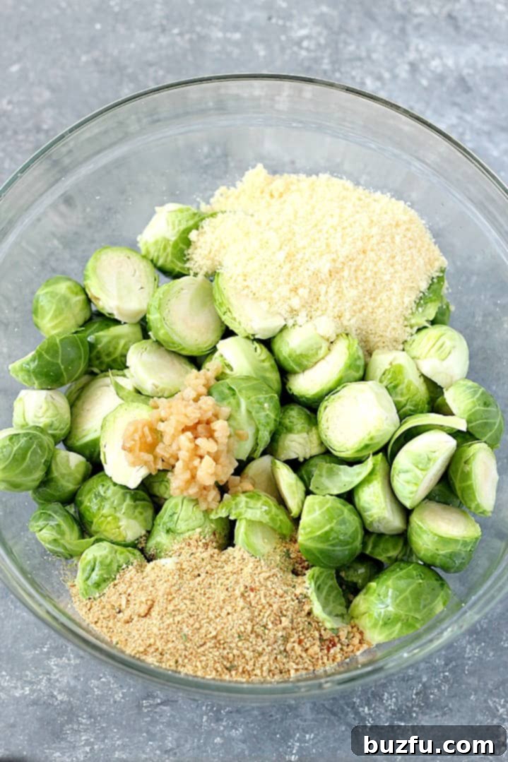 Ingredients for roasted Brussels sprouts in a glass bowl, including fresh sprouts, olive oil, garlic, Parmesan, and breadcrumbs.