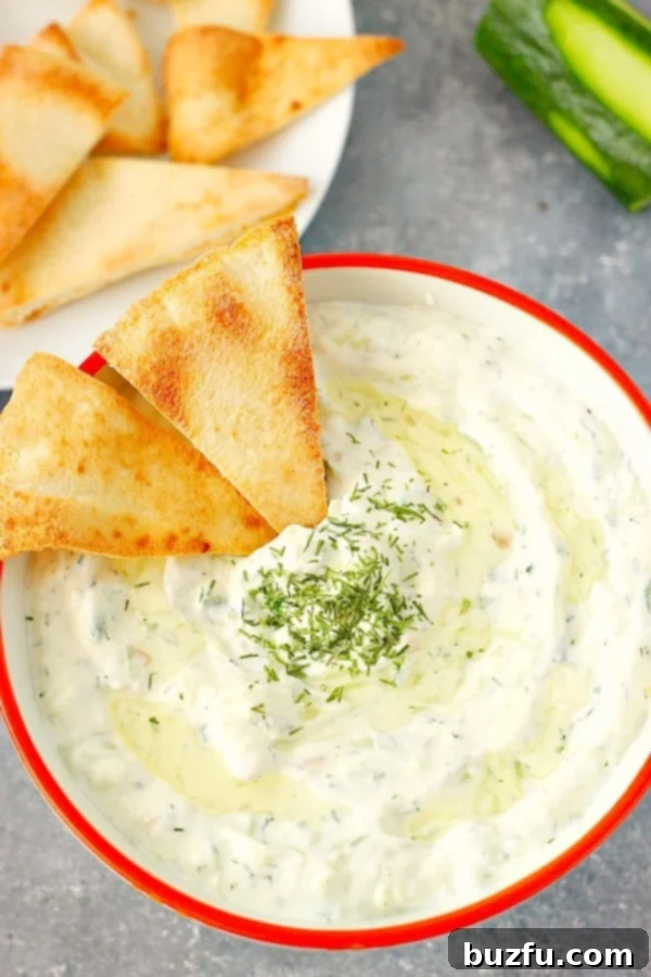 Easy Homemade Tzatziki Sauce - a creamy Greek yogurt dip with cucumber, garlic, and dill. Overhead shot of cucumber dip in bowl with red rim, showcasing the creamy texture and fresh ingredients.