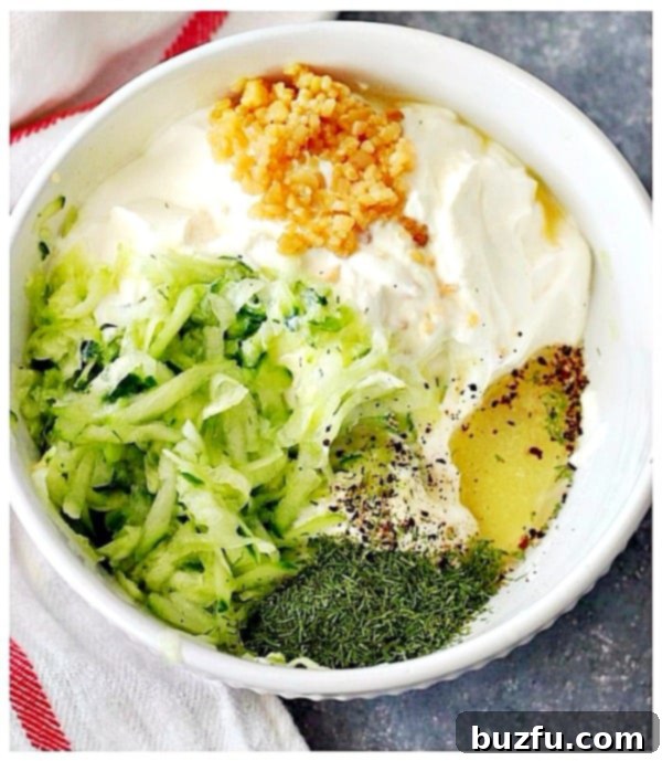 How to prepare the ingredients for homemade Tzatziki or Gyros sauce. Grated cucumber, garlic, sour cream, herbs and spices in bowl, ready to be mixed into a delicious Tzatziki sauce.