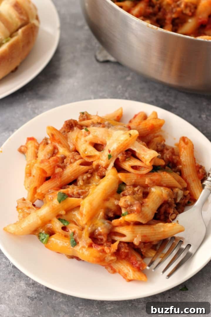Close-up of a portion of one-pot cheesy sausage penne, showing the melted cheese and a fork ready to serve.