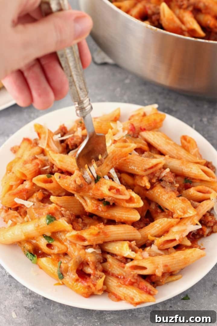 A large serving of one-pot cheesy sausage penne in a bowl, with melted cheese and basil garnish.