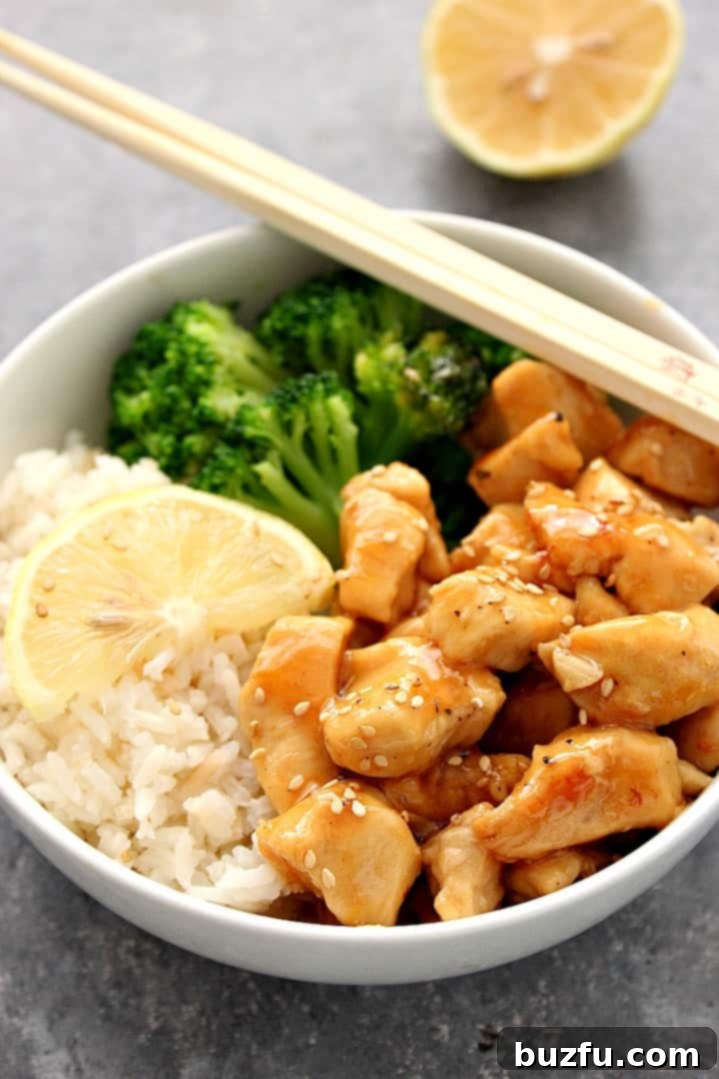 A close-up side view of a serving of Honey Lemon Chicken in a bowl, artfully arranged with steamed rice and bright green broccoli. Chopsticks rest casually on the rim, inviting a taste of this delectable meal.