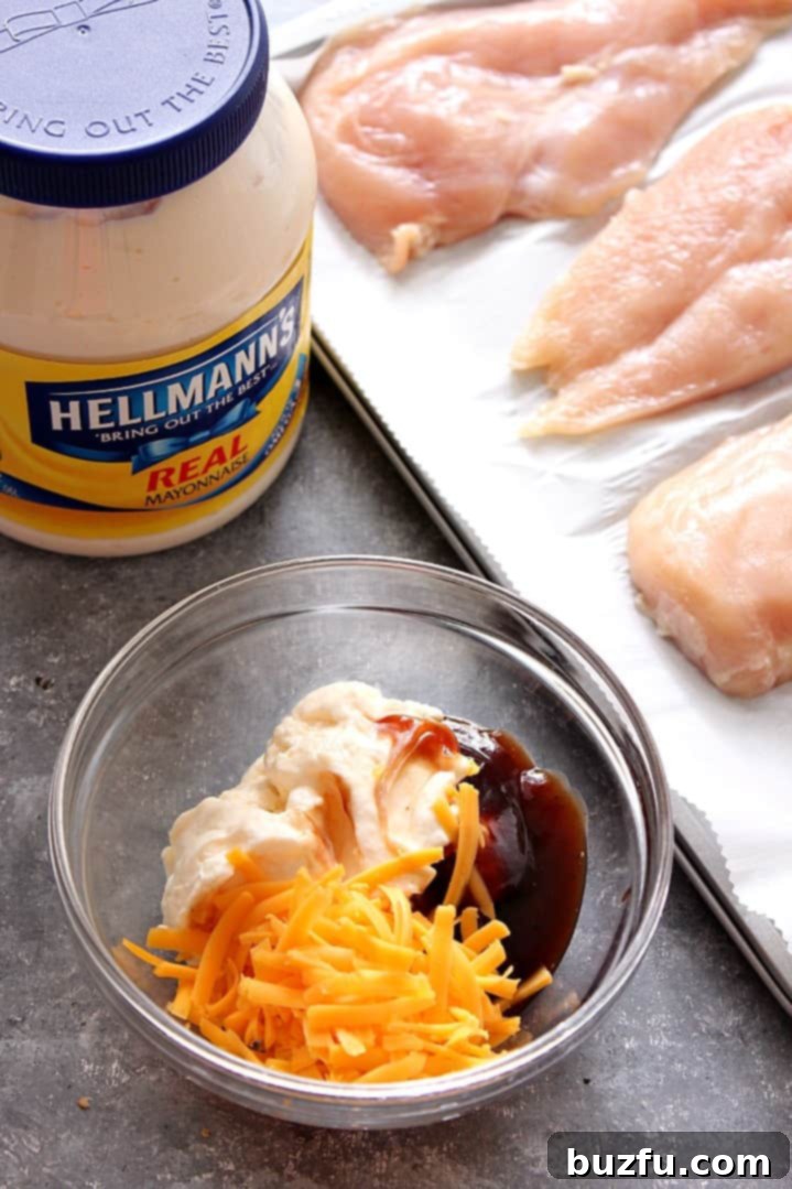 Overhead shot showcasing the simple ingredients for BBQ Cheddar Chicken: chicken breasts on a baking sheet, with separate bowls of mayonnaise, BBQ sauce, and shredded cheddar cheese ready for mixing.