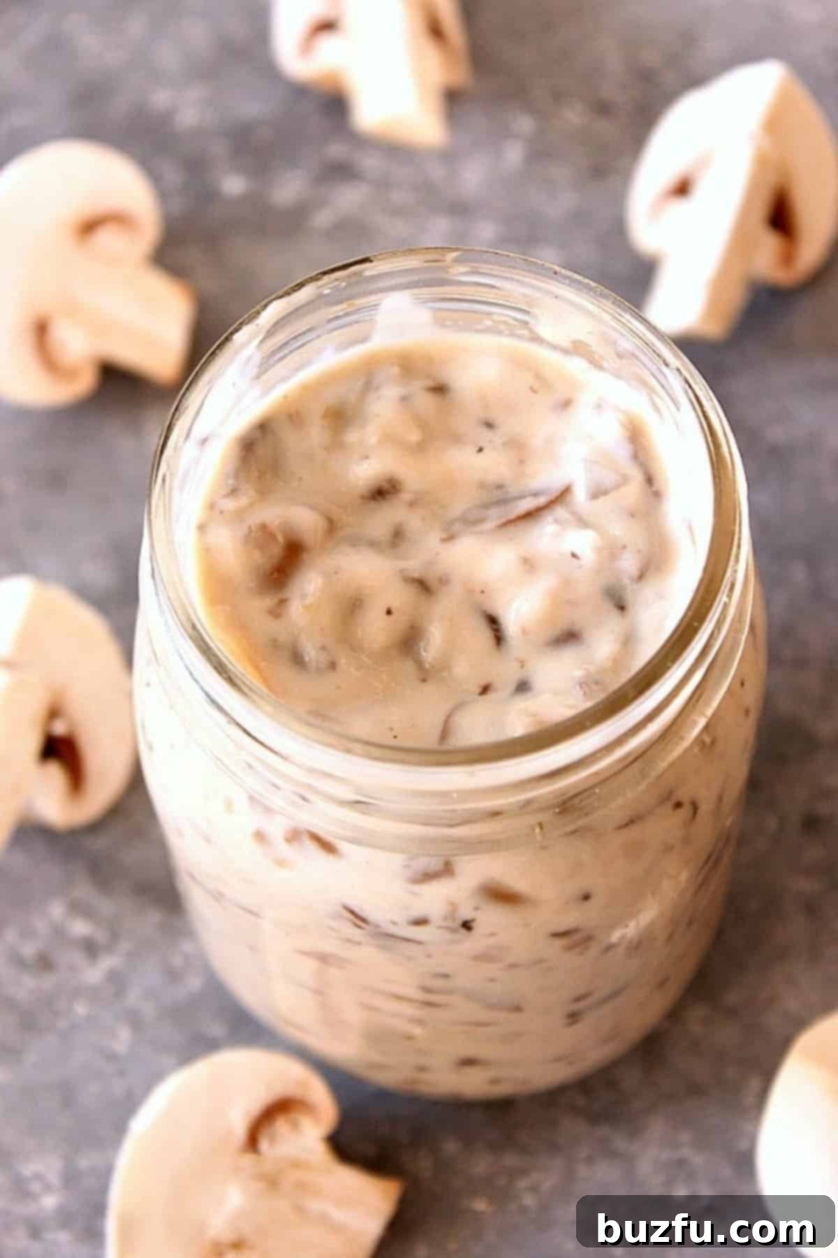 Craft Your Own Condensed Creamy Mushroom Soup 2 Cream of mushroom soup in a glass Mason jar, on a gray board with mushrooms around it.