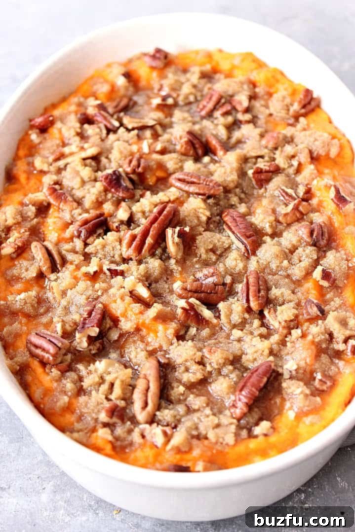 The Best Easy Sweet Potato Casserole Recipe - classic Thanksgiving holiday side dish made easy! www.crunchycreamysweet.com Close up shot of baked sweet potato casserole, topped with pecans and brown sugar.