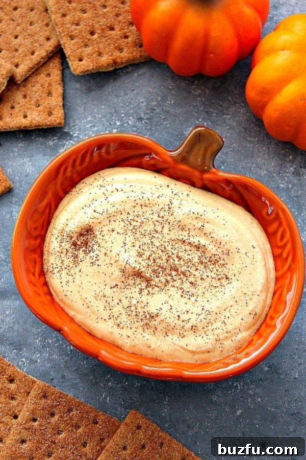 Creamy Pumpkin Cheesecake Dip - a perfect no-bake dessert for fall celebrations. Pumpkin cheesecake dip in an orange pumpkin-shaped serving bowl, garnished with a sprinkle of cinnamon.