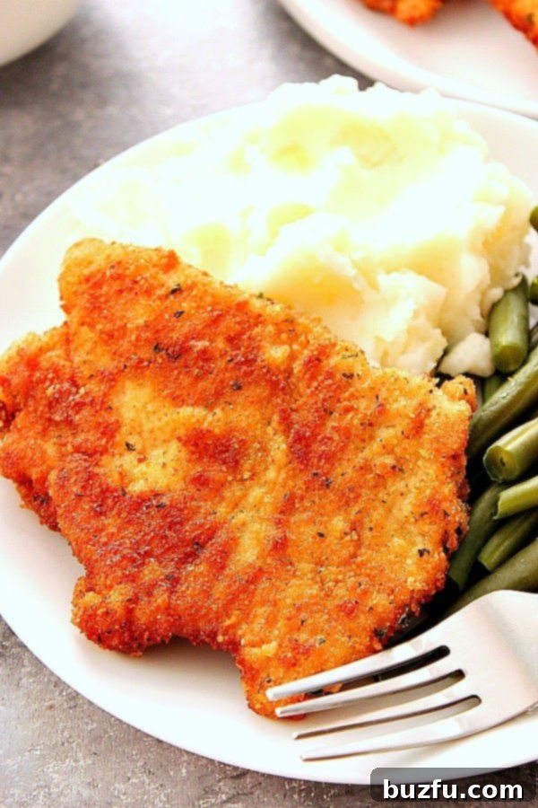 Pork schnitzel with mashed potatoes and green beans on white plate.