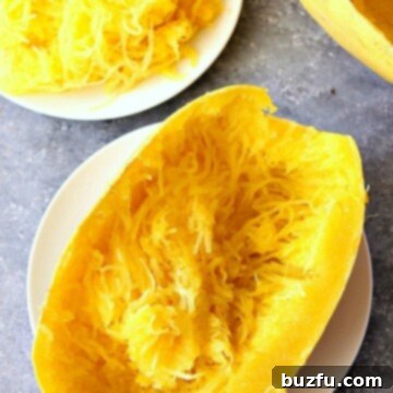 Instant Pot spaghetti squash half on white plate, ready to be shredded into healthy noodles.