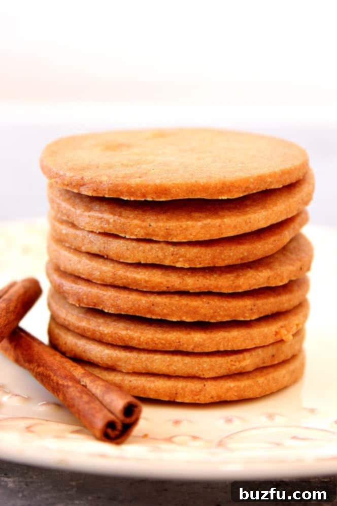 Stack of thin spiced shortbread cookies with cinnamon sticks on a wooden surface.