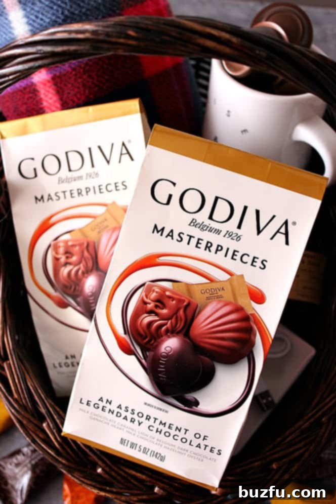 A guest welcome basket overflowing with comforts, including a plaid blanket, coffee mug, Godiva chocolates, and a notebook.