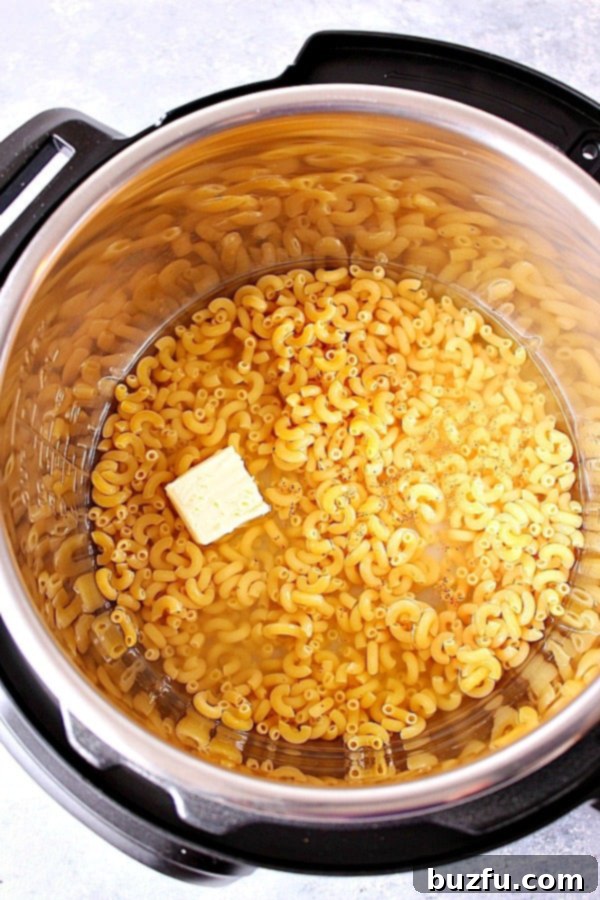 How to make creamy macaroni and cheese in the Instant Pot pressure cooker. Overhead shot of macaroni pasta in water, with pieces of butter on top, in Instant Pot. Shows the initial ingredients before pressure cooking.