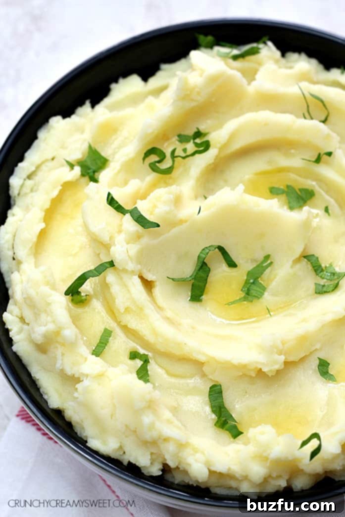 A close-up of fluffy, creamy slow cooker mashed potatoes in a white serving bowl, garnished with fresh herbs.