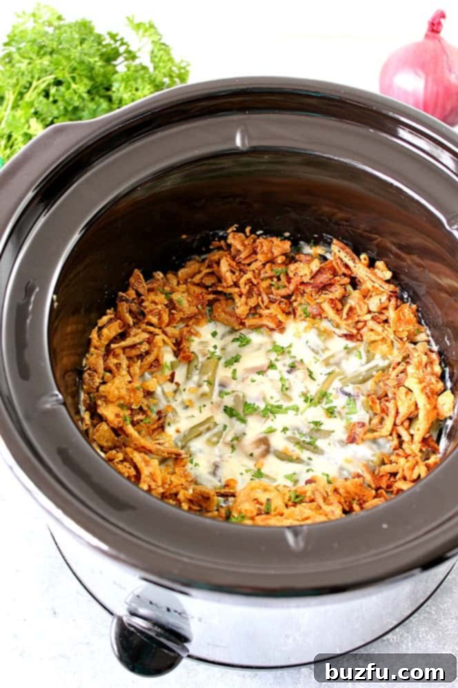 A serving of creamy slow cooker green bean casserole in a rustic white bowl, garnished with crispy fried onions.