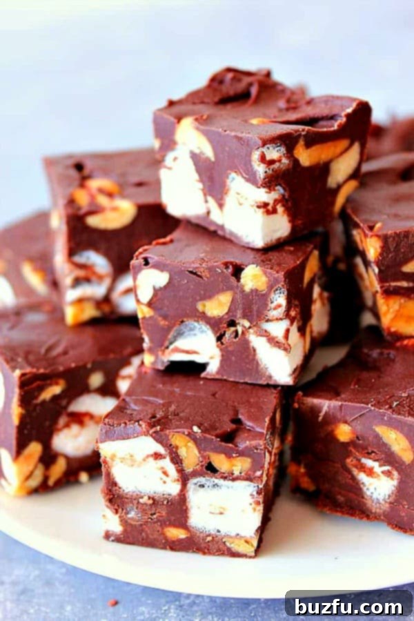 Rocky Road Fudge - chocolate fudge with mini marshmallows and peanuts. Easy sweet treat made with only 4 ingredients! Squares of chocolate fudge with peanuts and marshmallows on a white plate.