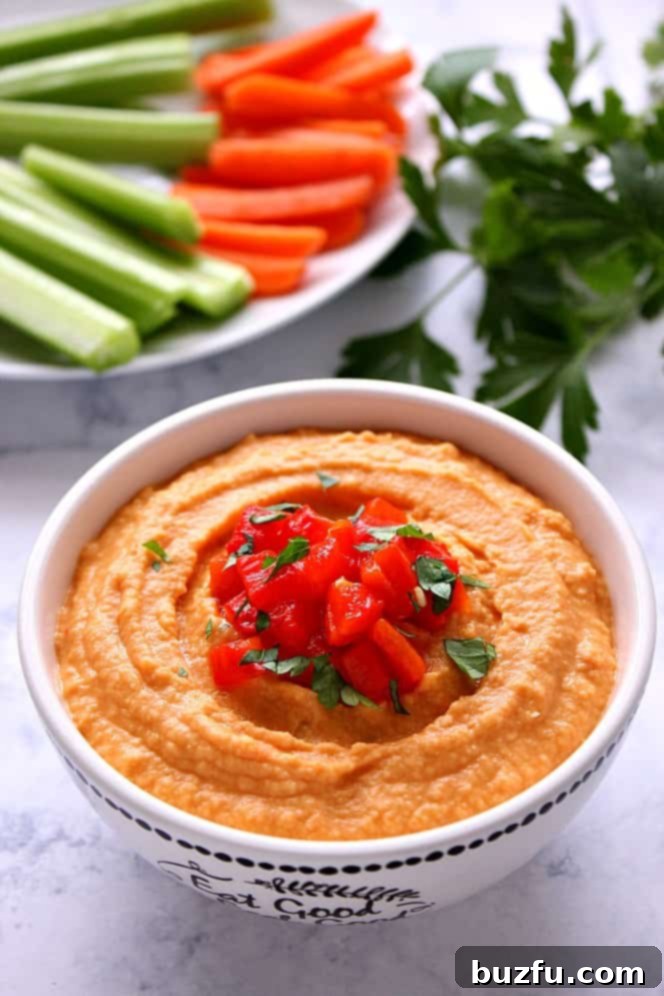 Freshly made Red Pepper Hummus garnished with finely chopped red peppers and a sprinkle of herbs, presented in a rustic bowl.
