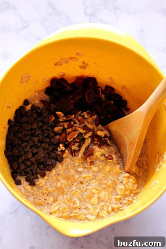 Easy Baked Oatmeal Cups Recipe - hearty and filling oatmeal baked into muffin cups. Perfect breakfast idea for busy days! Overhead shot of yellow mixing bowl with oatmeal, chopped nuts, dried cranberries and mini chocolate chips.