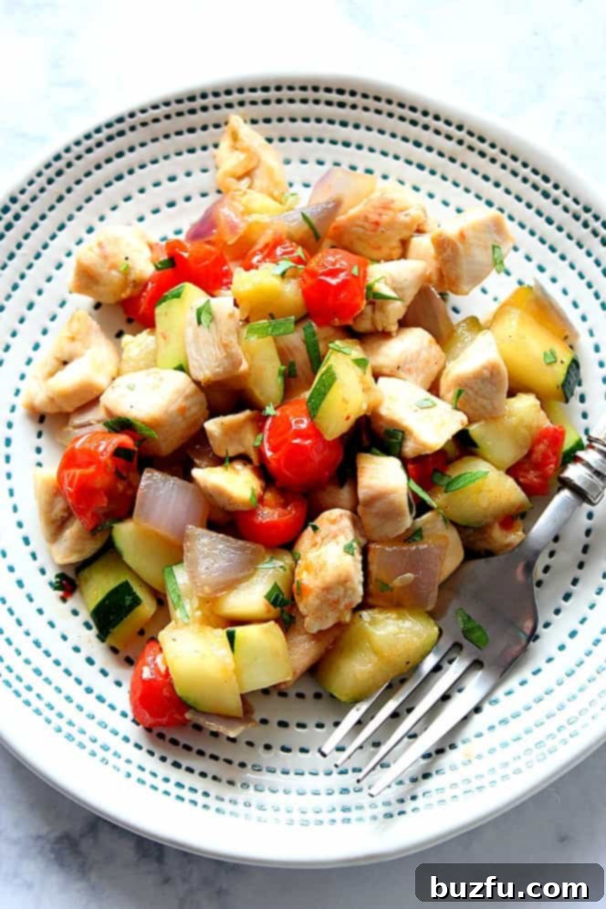 Healthy and colorful chicken and vegetable skillet served on a white plate, garnished with fresh herbs