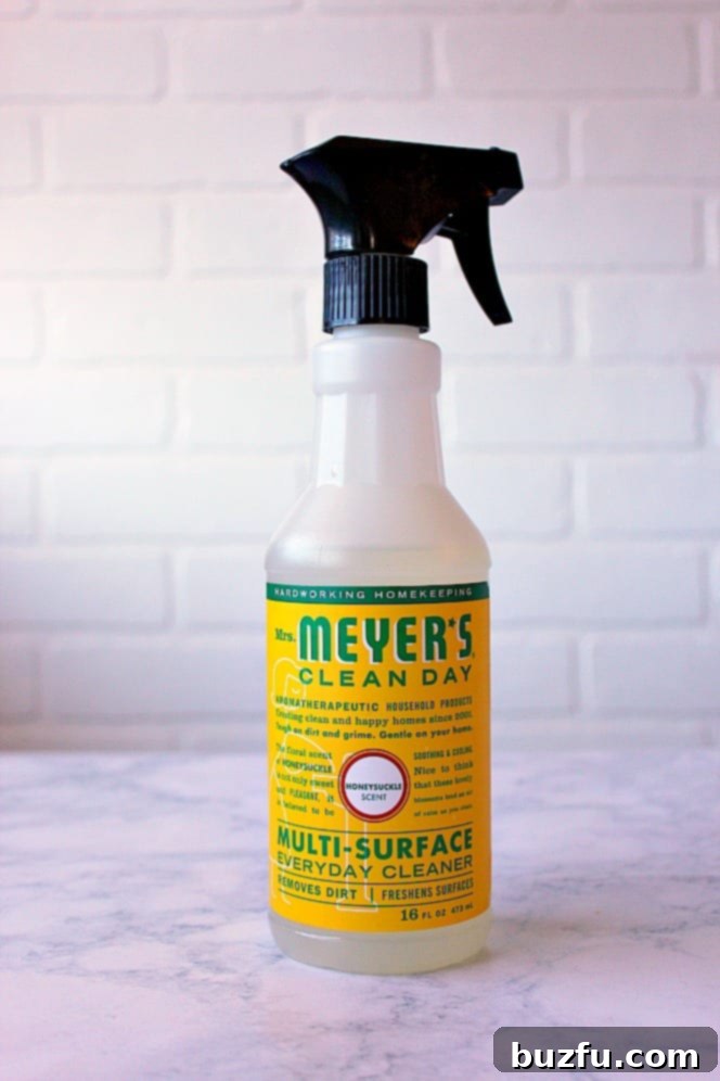 A bottle of Mrs. Meyer's Clean Day Multi-Surface Everyday Cleaner in Honeysuckle scent, with a fresh sprig of honeysuckle.