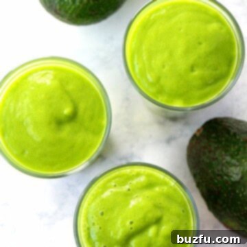 Radiant Avocado Elixir 2 Close-up shot of a glass of green Avocado Glow Smoothie with a straw, garnished with fresh fruit, inviting and refreshing.