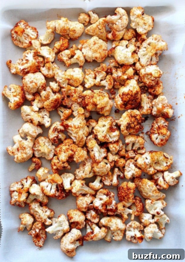 Roasted cauliflower florets generously seasoned with shawarma spices, spread evenly on a parchment-lined baking sheet, ready for the oven.