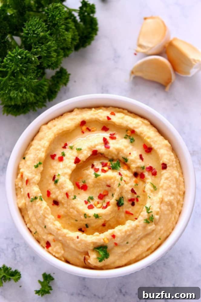 Velvety No-Tahini Hummus 2 A bowl of creamy, homemade hummus garnished with fresh parsley and a drizzle of olive oil, resting on a elegant marble board ready for serving.