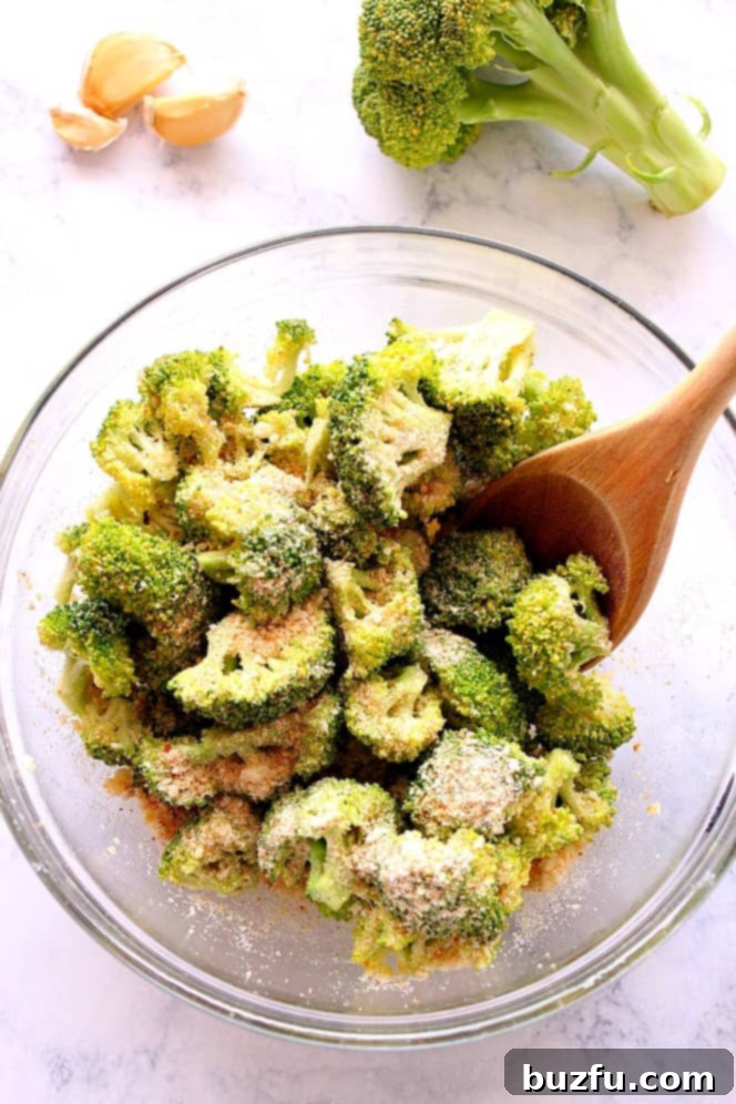 Broccoli florets coated in olive oil, garlic, and seasoning in a mixing bowl before roasting.