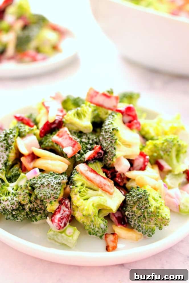 A serving of creamy broccoli salad on a white plate, garnished with fresh herbs.
