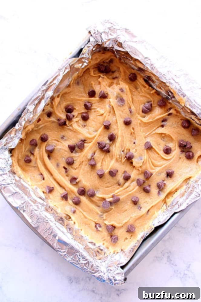 Blondie bar dough spread evenly in a parchment-lined baking pan, ready for the oven.