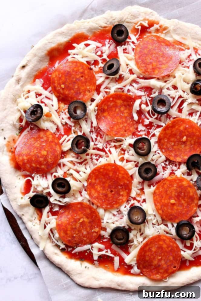 Delicious pizza dough topped with cheese, pepperoni, and black olives, ready for baking.