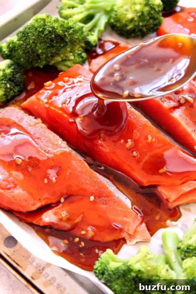 Drizzling teriyaki sauce over salmon and broccoli on a baking sheet.