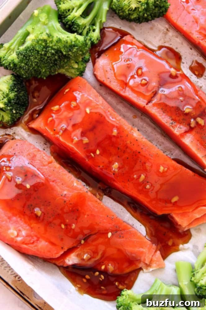 Raw salmon fillets and fresh broccoli on a parchment-lined baking sheet.