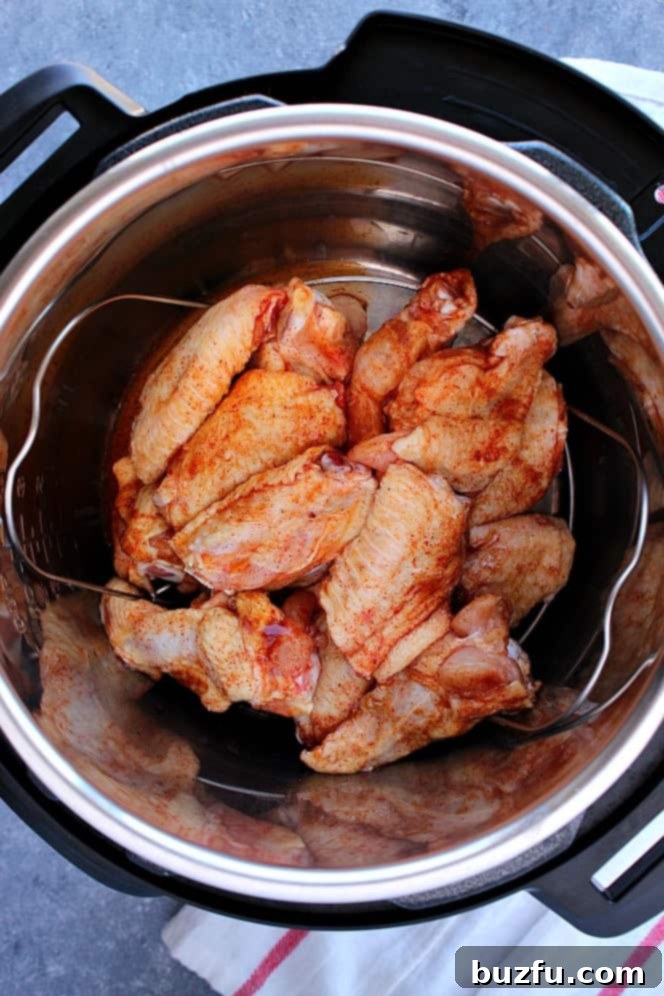 Instant Pot BBQ Chicken Wings Recipe - Juicy chicken wings with sweet and spicy rub, cooked to perfection in the Instant Pot, then coated in rich BBQ sauce and broiled for crispy skin. The pressure cooker helps cook them fast and keep them juicy. Chicken wings are being cooked inside the Instant Pot insert, illustrating the pressure cooking stage.
