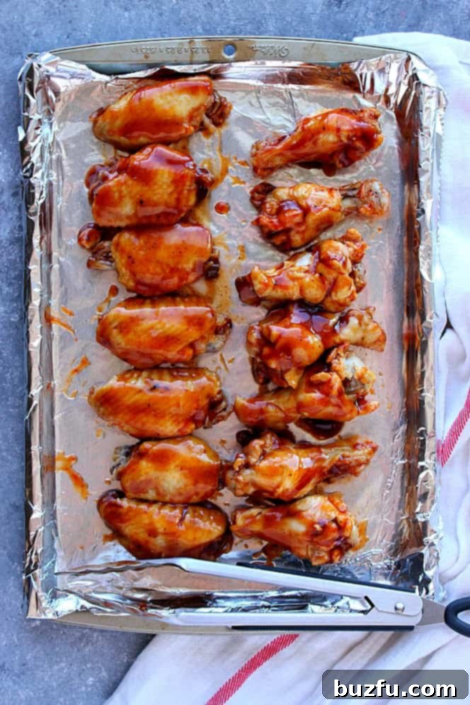 Instant Pot BBQ Chicken Wings Recipe - Juicy chicken wings with sweet and spicy rub, cooked to perfection in the Instant Pot, then coated in rich BBQ sauce and broiled for crispy skin. So tasty! Close-up of chicken wings richly coated in BBQ sauce and arranged on a baking sheet, ready for broiling to achieve perfect caramelization.
