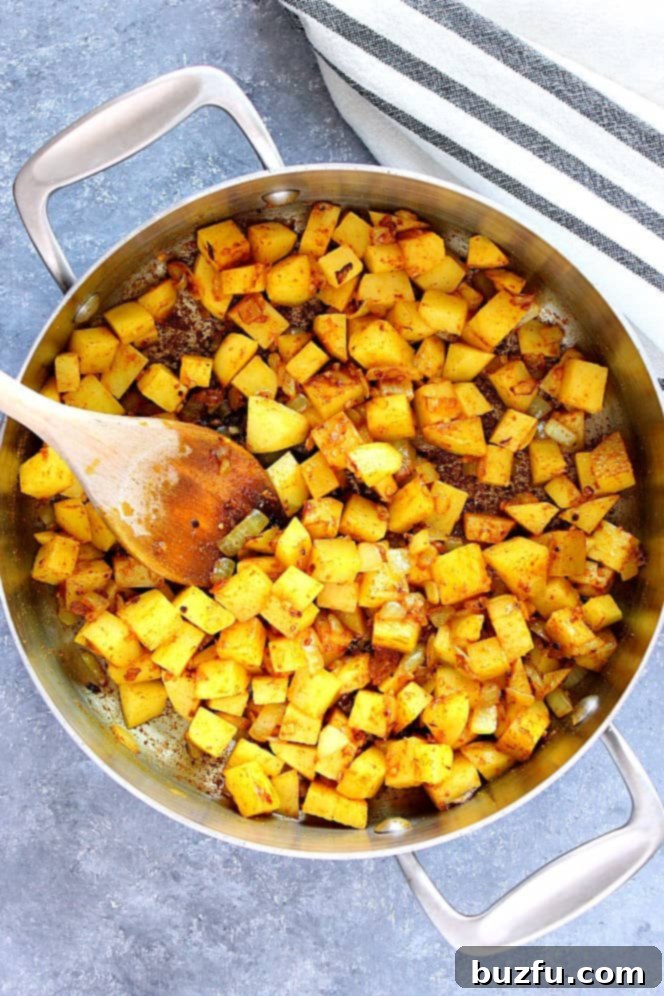 Diced potatoes being sautéed with curry spices in a stainless steel pan