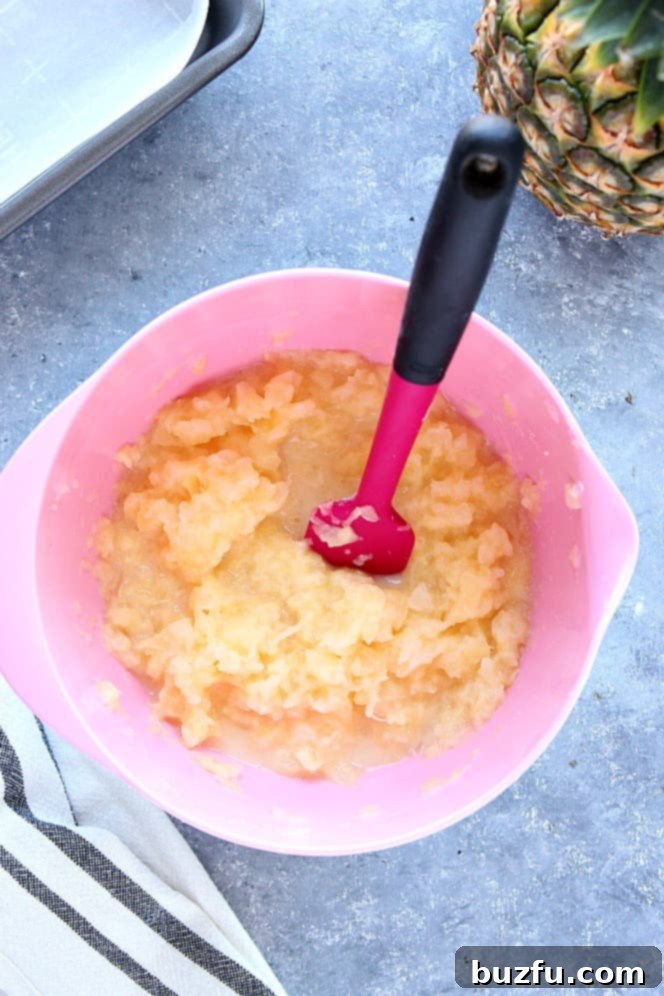 A vibrant bowl of crushed pineapple filling, expertly mixed with sugar and cornstarch, sits ready with a pink spatula, highlighting its rich texture and bright color.